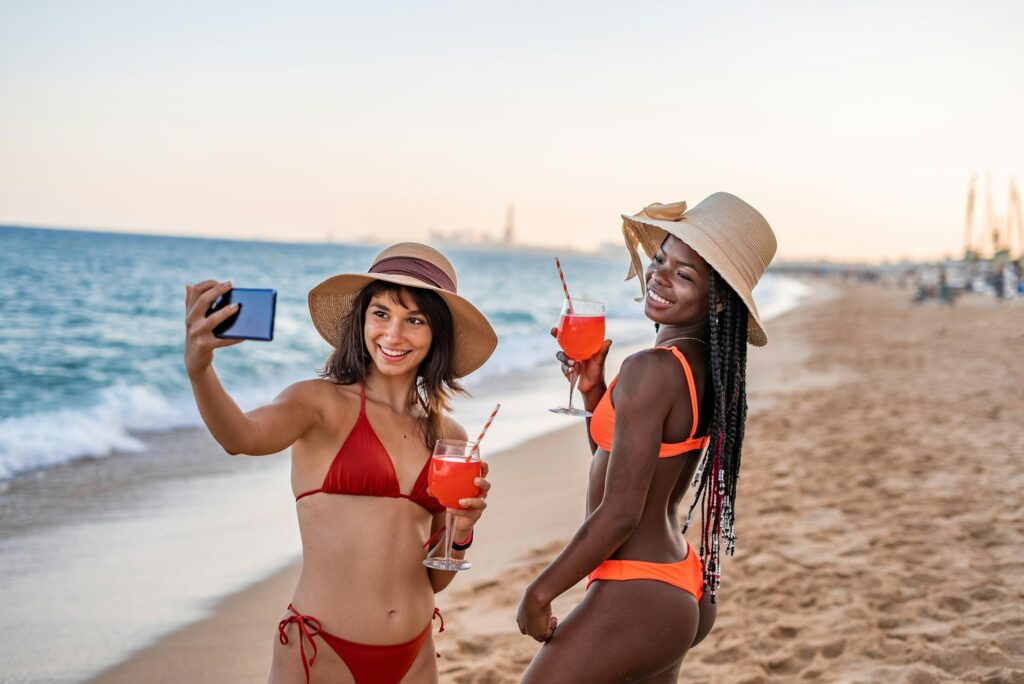 Happy multiracial girlfriends taking selfie on beach