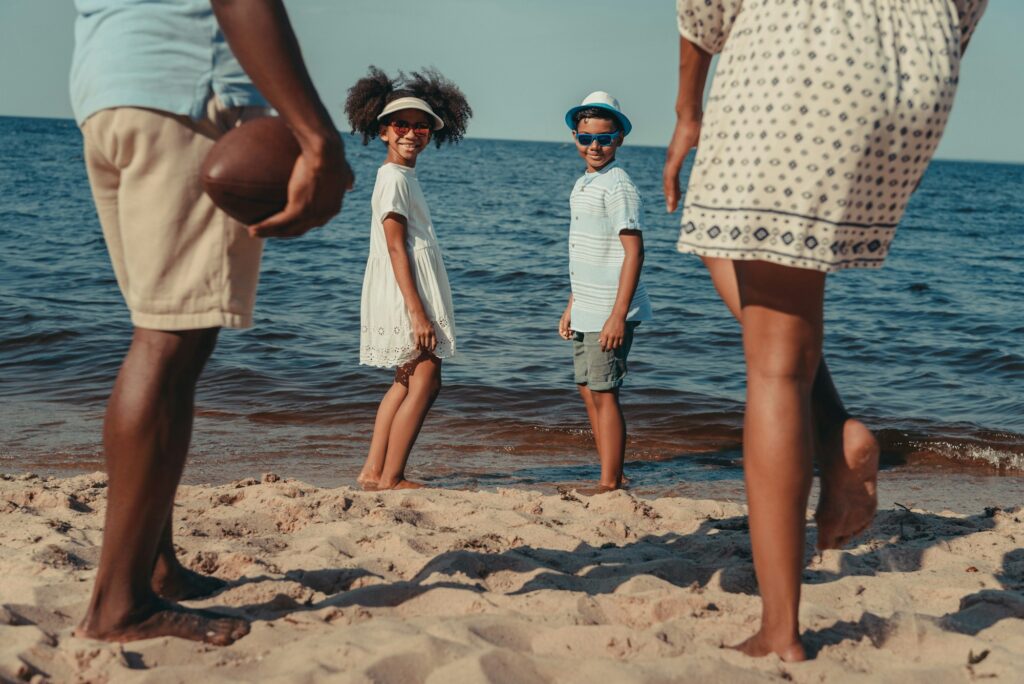 cropped shot of african american family with two children playing with rugby ball on beach